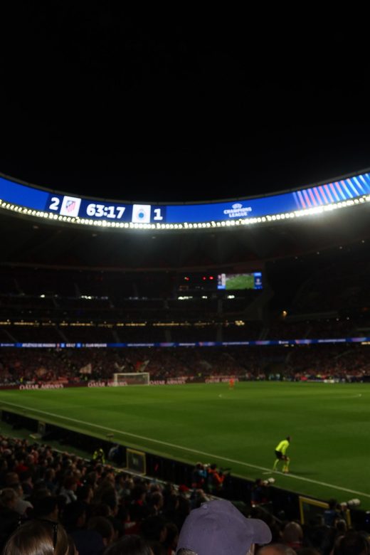 Stadium scoreboard showing Atlético de Madrid 2, Club Brugge 1, seen from the stands