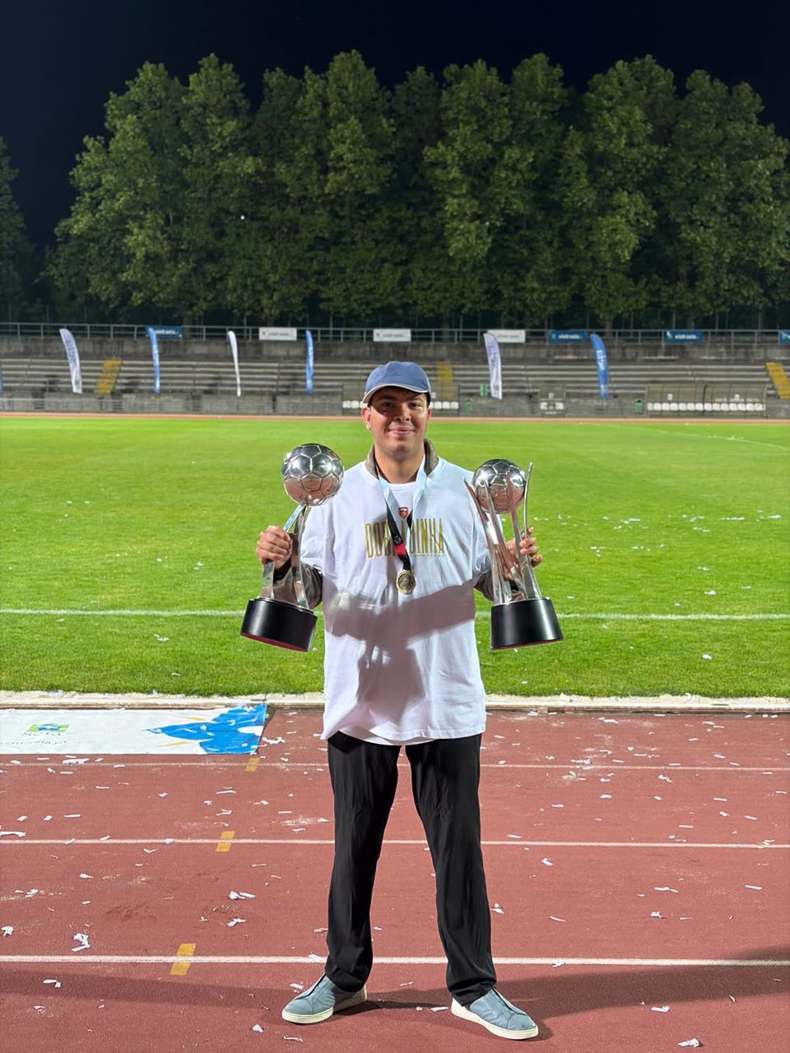 Jai Agarwal standing on the running track of the Estádio Municipal da Guarda holding two trophies